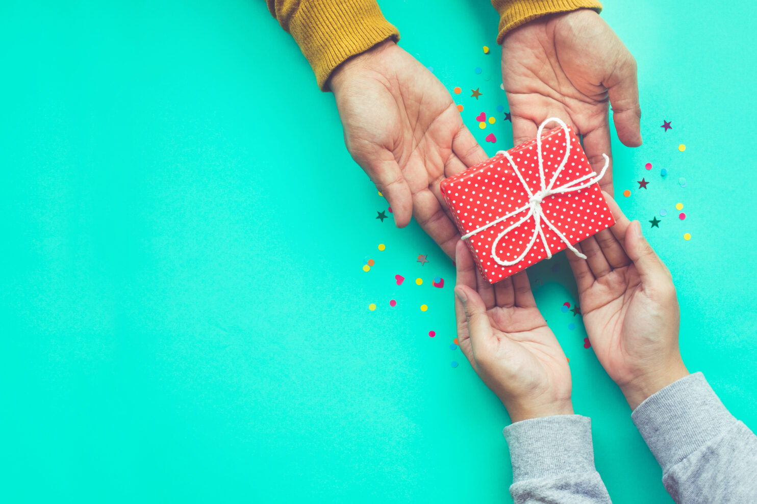 Adult handing a child a small red package as a gift.