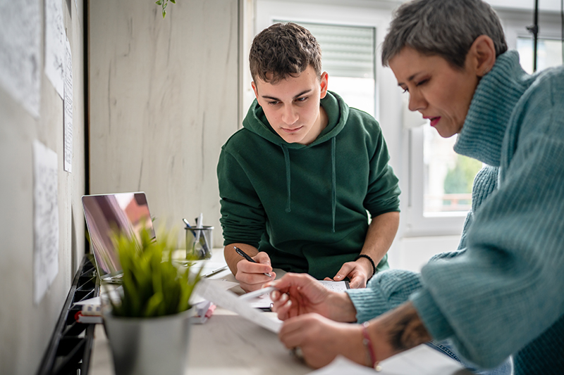 One student teenage caucasian man learning with help of his tutor professor or mother senior woman at home having private lesson