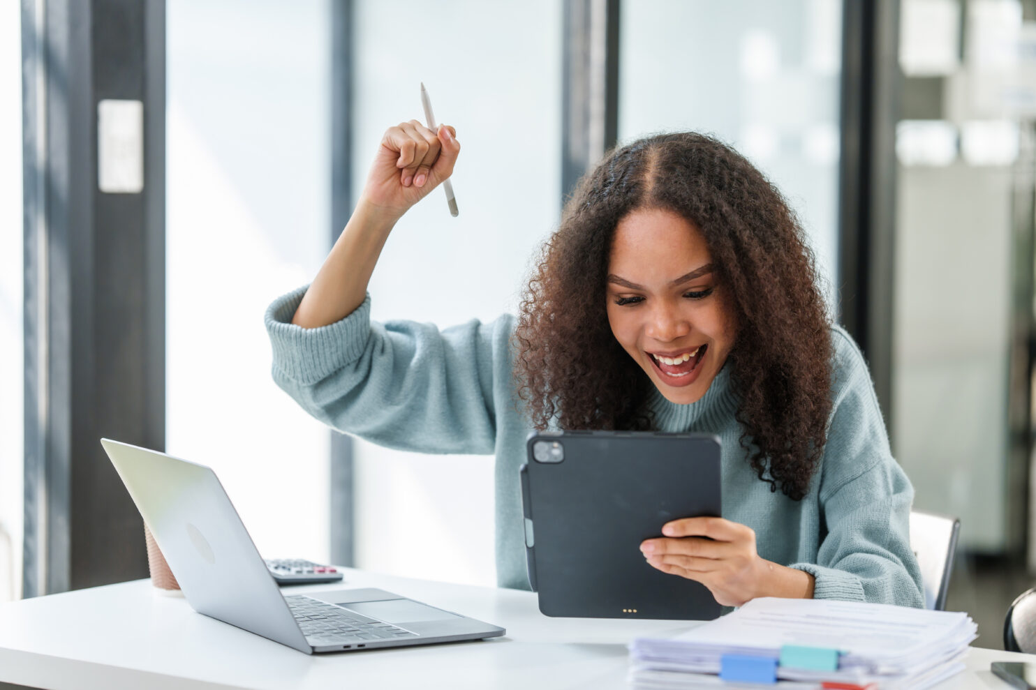 elated African American university student, celebrating a successful moment, holding a tablet and a pen aloft.